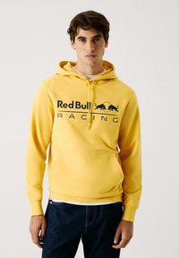 Felpa gialla realizzata in tessuto morbido, con tasca a marsupio, cappuccio regolabile e un grande logo "Red Bull Racing" in nero.