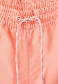 Gros plan sur une ceinture élastique corail rose avec des détails cousus et un cordon tressé blanc et rose noué.