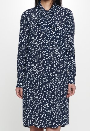 Robe chemise bleu marine avec un motif à pois blancs, dotée d'un col à nouer, de manches longues et d'une fermeture à boutons sur le devant. Tissu doux et coupe décontractée.