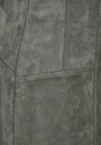 Gråmocka med en slät textur, synliga sömmar och en strukturerad form, inklusive en sidofickdetalj.