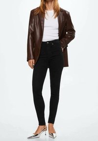 Černé skinny džínsy s vysokým pasem v kombinaci s přiléhavým bílým trikem a hnědým sako z umělé kůže, doplněné stříbrnými špičatými podpatky.