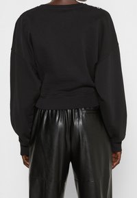 Černá krátká mikina s klesajícími rameny a kulatým výstřihem. Kombinována s lesklými černými kalhotami z koženky, které mají hladkou texturu.