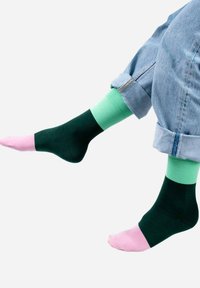 Skarpetki w wielu kolorach, z ciemnozielonymi, miętowymi i jasnoróżowymi sekcjami. Gładka tekstura; kontrast między kolorami jest wyraźny.