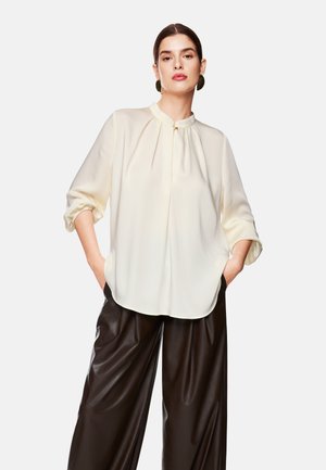 Ivory blouse with a Mandarin collar, pleated detail, and roll-up sleeves, paired with glossy black leather wide-leg trousers.