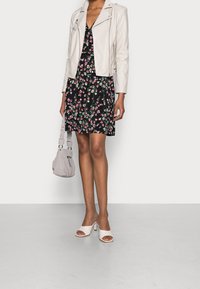 Vit läderbikerjacka över en svart blommig klänning. Grå handväska och öppna vita klackar fulländar outfiten.