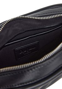 Intérieur d'un sac en cuir noir avec une doublure en tissu, doté d'une fermeture éclair et d'une étiquette de marque en cuir à l'intérieur. Texture lisse et design minimal.