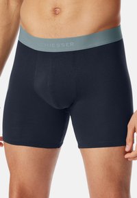Zwarte boxershorts van zacht katoen met een lichtgrijze elastische tailleband waarop de merknaam "SCHIESSER" bovenaan gedrukt staat.