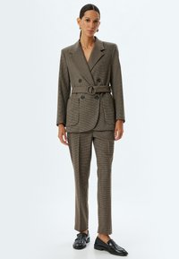 Braun kariertes Tailliertes Blazer mit passender Hose, Gürteldetail in der Taille und schwarzen Loafers. Glatte Textur, strukturiertes Design.