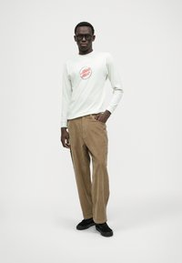 Long-sleeve cream t-shirt with red graphic, paired with tan corduroy wide-leg pants. Black sneakers complete the outfit.