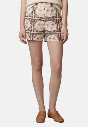 Femme portant un short taille haute avec un imprimé palmiers marron et beige, associé à des mocassins couleur cuir clair et un haut couleur crème.