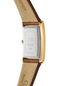 Reloj rectangular de acero inoxidable con caja en tono dorado, correa de cuero marrón y forro beige. La parte posterior presenta la marca grabada y sus especificaciones.
