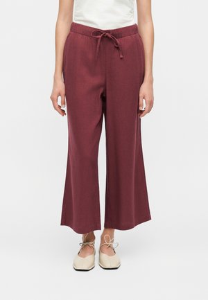 Pantalon large bordeaux avec taille à cordon, porté avec des ballerines crème à bout carré sur une personne debout.