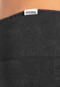 Zwarte sportlegging met een gestructureerde ribbels tailleband en een gladde onderkant, voorzien van een klein wit merketiket met de tekst "SMILODOX."