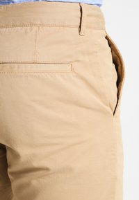 Pantalon beige clair en tissu lisse, avec un design simple, doté d'une poche arrière et d'une poche latérale pour plus de praticité.