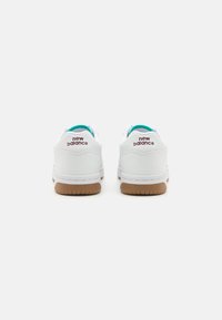 Weiße Sneakers mit einem Obermaterial aus glattem Leder, türkisfarbener Innensohle, gepolstertem Kragen und einer braunen Gummisohle mit einem strukturierten Muster.