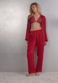 Rode satijnen pyjama set met een kant bra en losse broek met een elastische tailleband. Soepele textuur en eenvoudige uitstraling.