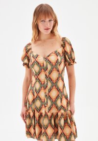 Robe à boutons sur le devant avec un motif de diamants dans des couleurs orange, verte et crème. Manches courtes bouffantes et ourlet évasé.