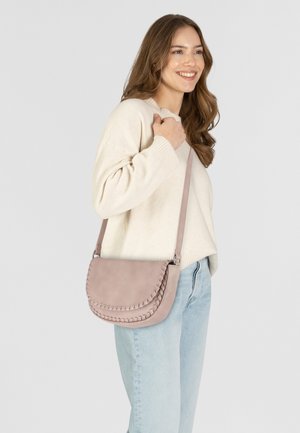 Borsa a tracolla in morbido pelle rosa chiaro con design a patta curvata, adornata da un dettaglio intrecciato e una lunga tracolla regolabile, indossata sopra un maglione chiaro.