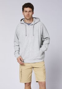 Gray zip-up hoodie with a drawstring hood, featuring a small logo on the chest. Worn with beige cargo shorts, showcasing pockets and a relaxed fit.
