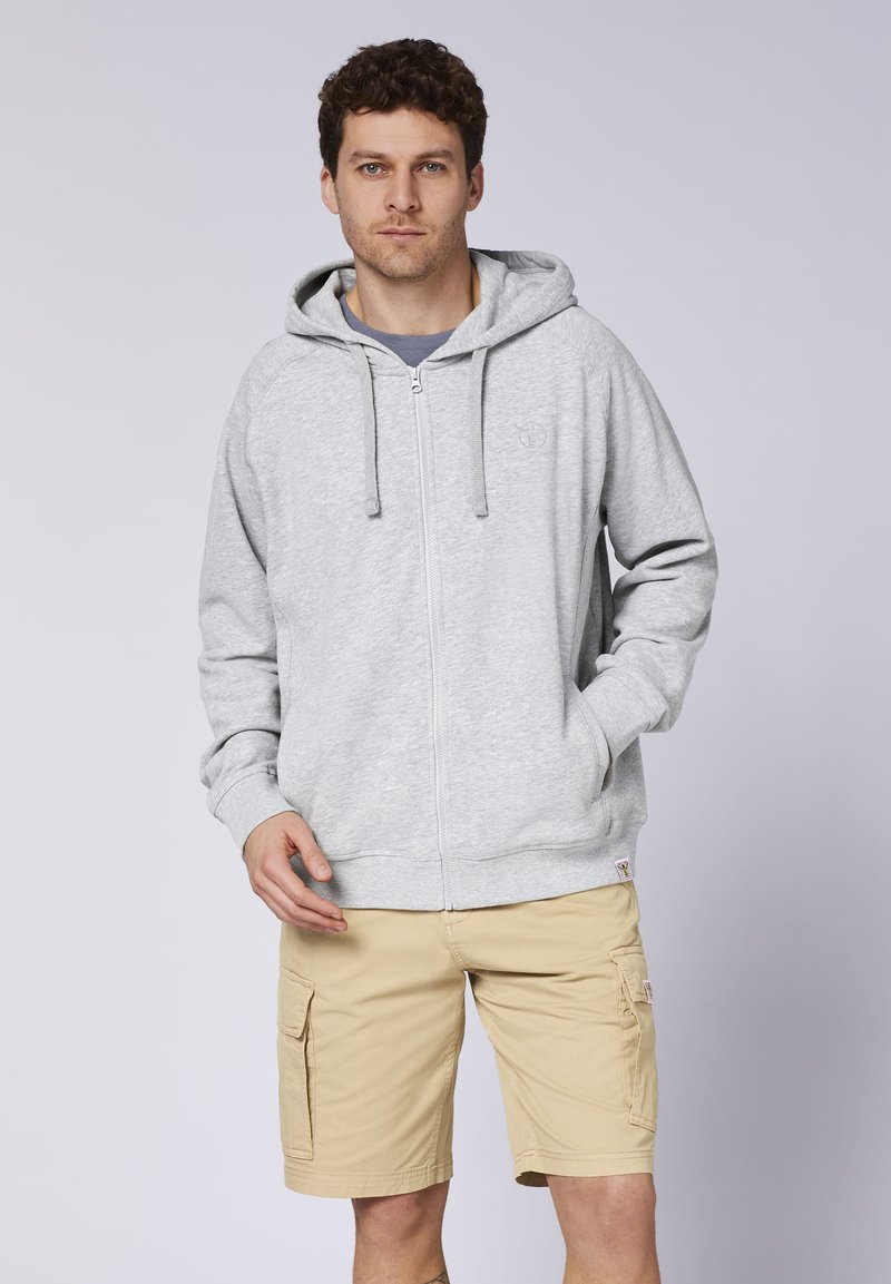 Gray zip-up hoodie with a drawstring hood, featuring a small logo on the chest. Worn with beige cargo shorts, showcasing pockets and a relaxed fit.