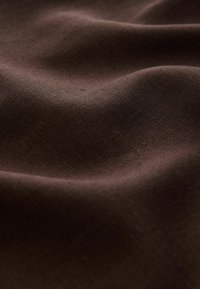 Tissu doux marron foncé avec une texture visible et des plis subtils créant de douces ondulations à la surface.