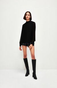 Top lungo a maniche lunghe plissettato nero con collo alto, abbinato a pantaloni in pelle neri e stivali con tacco alti fino al ginocchio. Texture liscia, design minimalista.