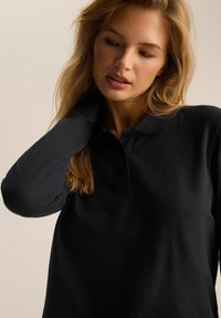 Czarny longsleeve polo z kołnierzykiem i małym haftowanym logo na klatce piersiowej. Teksturowany materiał z elegancką, dopasowaną sylwetką.