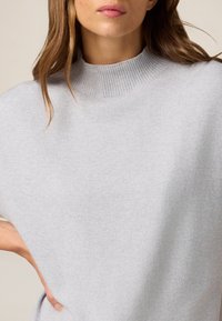 Light gray sweater with a ribbed high neck, loose fit, and soft texture, showing draping details. Simple and clean design.