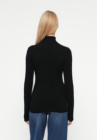 Top de malha preto de mangas longas com colarinho alto, silhueta justa e uma textura suave, combinado com jeans azuis de perna larga.