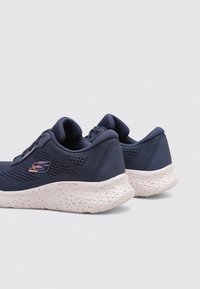 Zapatillas deportivas en color navy con parte superior de malla y textil, presentando una suela blanca moteada, un sutil detalle de logo y un collar acolchado para mayor comodidad.
