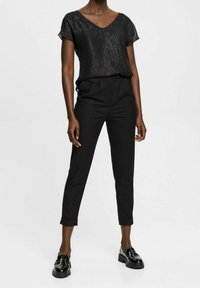 Černé tričko s krátkým rukávem a výstřihem do V s texturovaným povrchem, spárované s ušitými černými kalhotami. Dokončeno lesklými černými mokasíny.