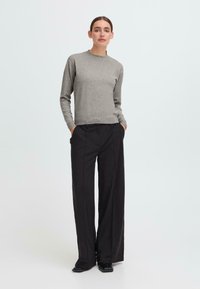 Gray knitted sweater with long sleeves and round neck, paired with high-waisted black wide-leg trousers and black shoes.