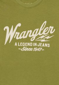 Žalias medvilninio marškinėlių su ryškiu baltu užrašu "Wrangler A Legend in Jeans Since 1947". Švelni tekstūra su apvaliu iškirpimu.