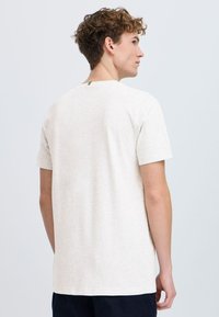 Camiseta de manga corta gris claro, hecha de una tela suave, con un escote redondo y un pequeño detalle de logo en la parte posterior. Corte relajado.
