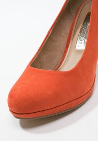 Gros plan sur la partie avant d'une chaussure pour femmes en suède orange avec un bout arrondi et une doublure intérieure beige.