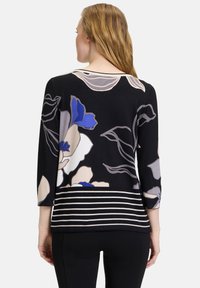 Schwarzer Pullover mit großen Blumenmustern in Blau-, Creme- und Grautönen, abgerundet durch gestreifte Akzente am unteren Rand und Dreiviertelärmel.