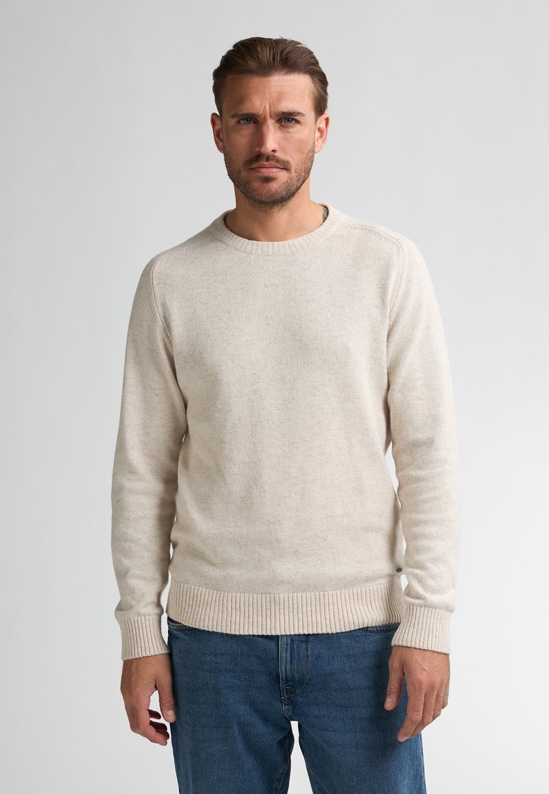 Crème-kleurige trui van textuurstof, met een ronde halslijn en ribgebreide manchetten en onderrand. Gedragen met blauwe denim jeans.