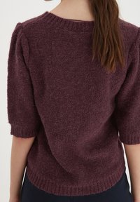 Burgundy stickad tröja med korta ärmar, texturerad yta, ribbad halsringning och manschetter, mjukt material och något lös passform.