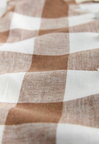 Tessuto a quadretti marrone e bianco con una trama ruvida, mostrato in primo piano con pieghe morbide e illuminazione naturale.