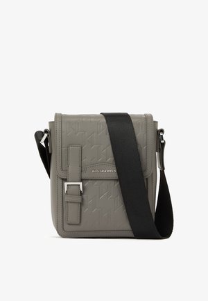 Bolso cruzado gris con patrón geométrico en relieve, forma estructurada, tapa frontal, asa ajustable negra y acentos en hardware plateado.