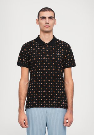 Black polo shirt with orange geometric pattern, short sleeves, and a black collar, worn with light blue pinstriped trousers.