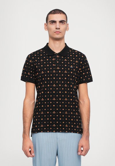 Camisa polo negra con un patrón geométrico naranja, de mangas cortas y con un cuello negro, combinada con pantalones de rayas finas en azul claro.