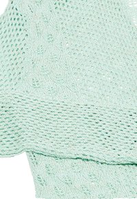 Material tricotat de culoare verde mentă, cu o țesătură deschisă și un model texturat, având o margine ondulată și o bordură netedă la partea de jos.