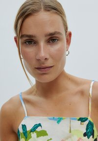 Bloemmotief jurk met vierkante halslijn en dunne bandjes. Heeft groene en blauwe bladeren op een lichte achtergrond. Gladde textuur.
