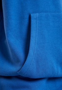 Sudadera azul con una textura suave, un bolsillo tipo canguro en el frente y un dobladillo acanalado. El material parece grueso y acogedor, ideal para uso casual.