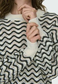 Maglione lavorato a maglia con motivo a onda in crema e nero, dotato di polsini a costine e una trama aperta testurizzata. Design leggero e aderente.