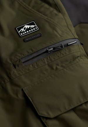 Oliwkowa kurtka z fakturowanej tkaniny, z kieszenią na zamek błyskawiczny oraz naszywką z logo gór. Wytrzymała konstrukcja z wzmocnionymi szwami.