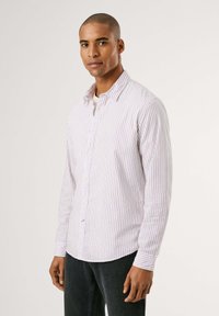 Camisa de manga larga a rayas en color púrpura claro y blanco, hecha de algodón, con cierre de botones y un dobladillo redondeado. Combinada con jeans oscuros.