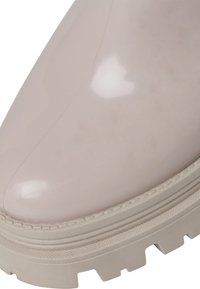 Bottine glossy rose clair avec un bout rond, semelle beige texturée et détails de couture subtils sur la tige.