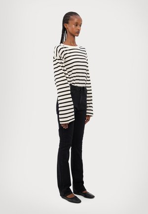 Camisola de mangas longas às riscas em creme e preto, combinada com jeans pretos e sapatos planos. A camisola apresenta mangas largas e um corte descontraído.
